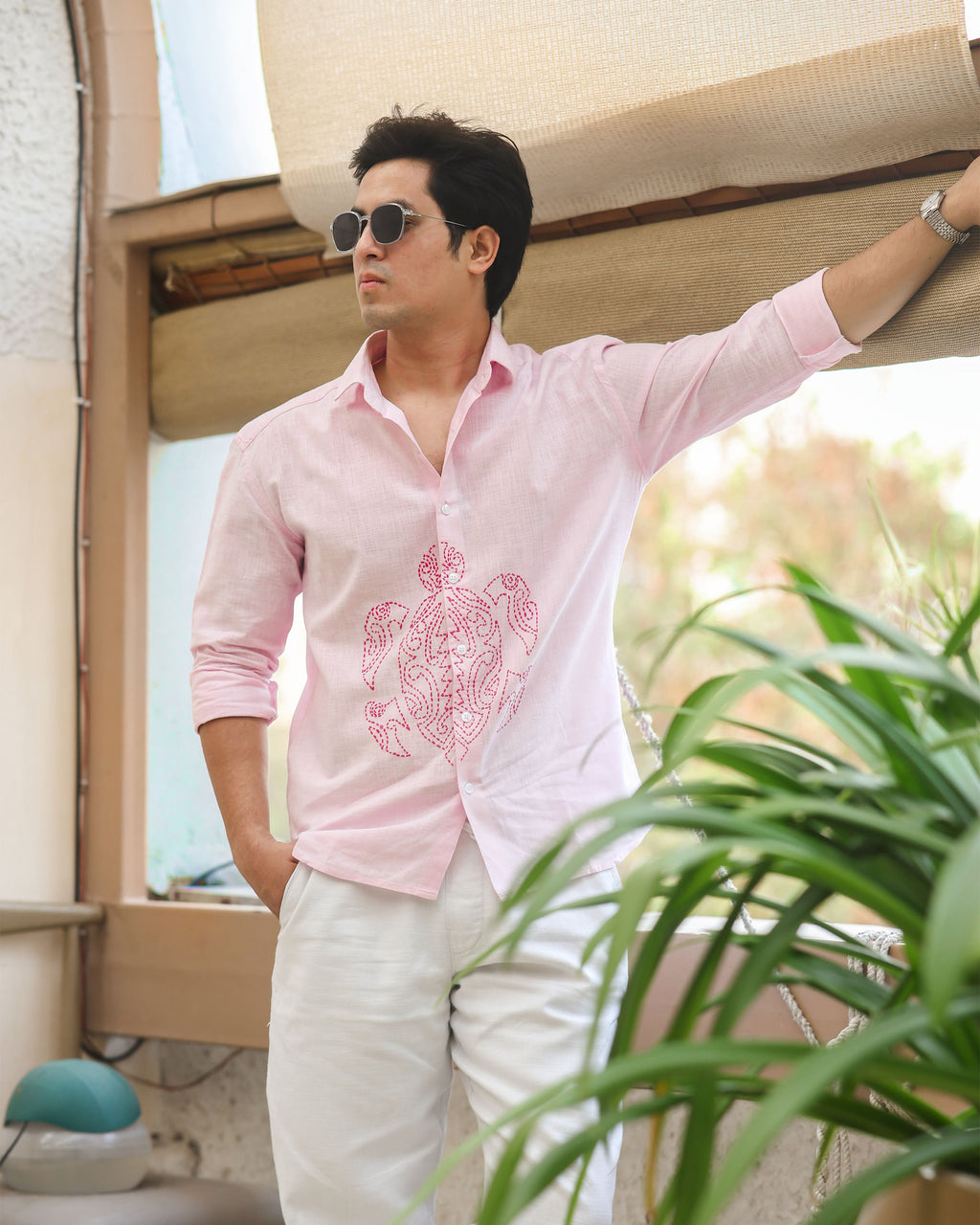 Man wearing a pink shirt with a floral design and sunglasses, standing in an outdoor setting.