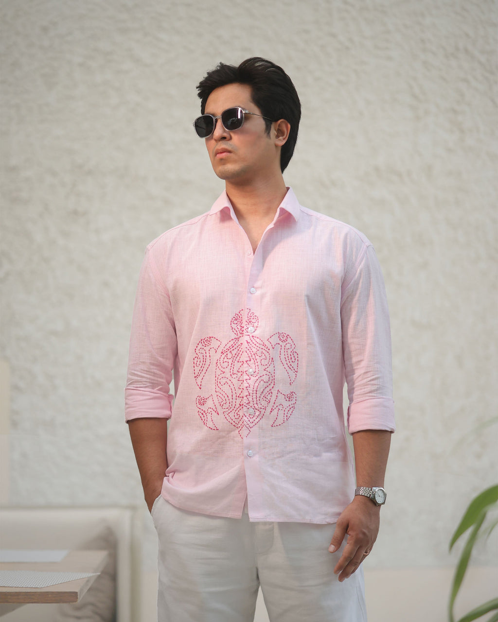 Man wearing a light pink linin shirt with a turtle design and white pants against a plain background