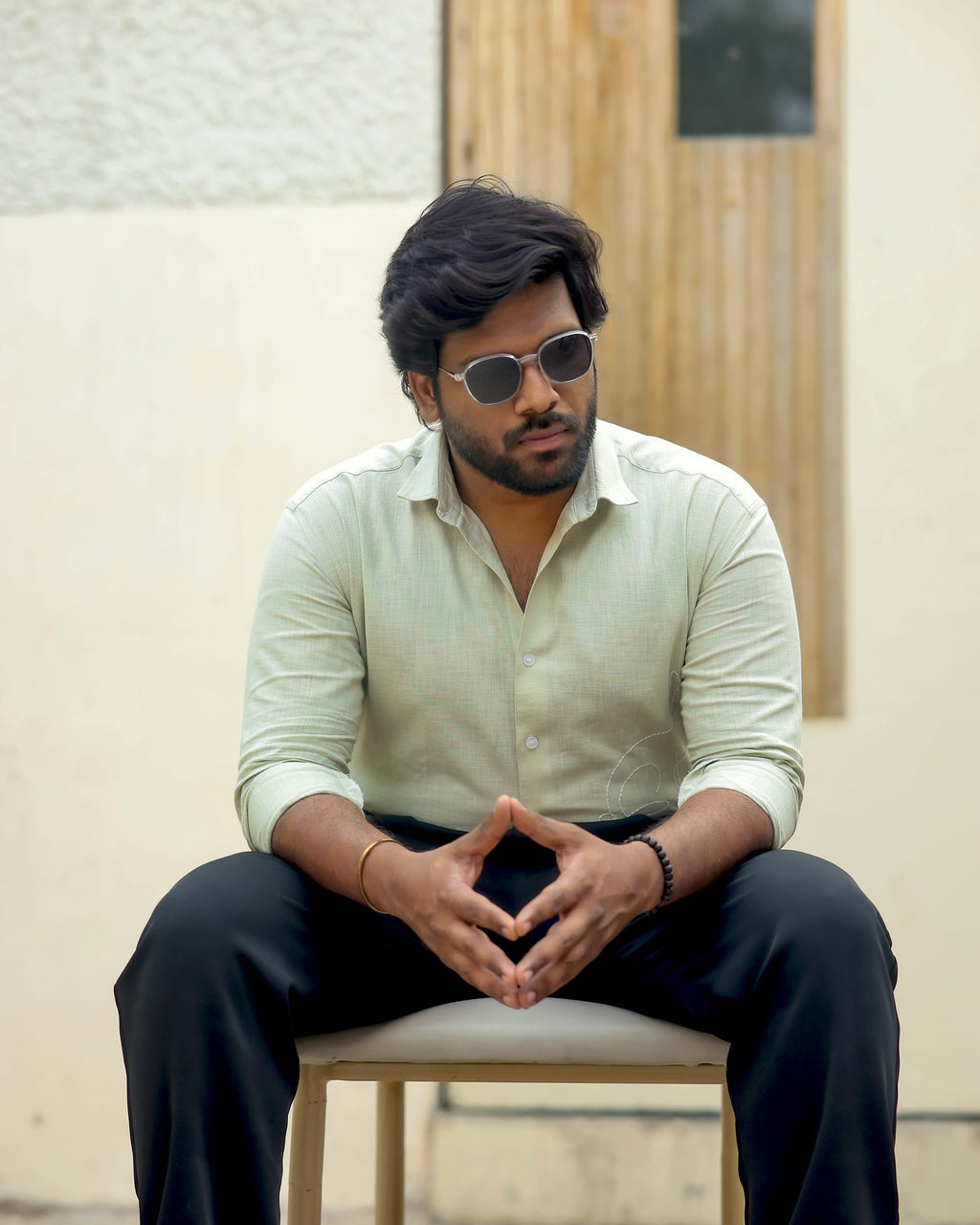 Man sitting on a chair wearing sunglasses and a light shirt with dark pants.