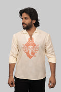 A man wearing a cream-colored linen long-sleeve shirt with a prominent orange Ganesha graphic on the front, paired with black pants, set against a solid gray background.